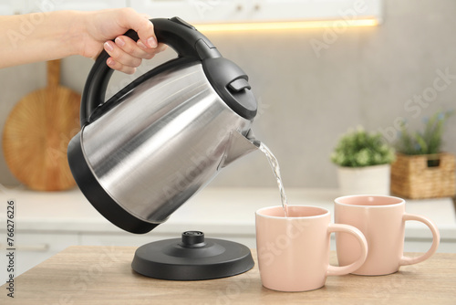 Valokuva Woman pouring hot water from electric kettle into cup in kitchen, closeup