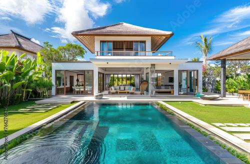 A photo of the front view of an elegant and modern Bali-style villa with a big garden, concrete walls, swimming pool © Kien