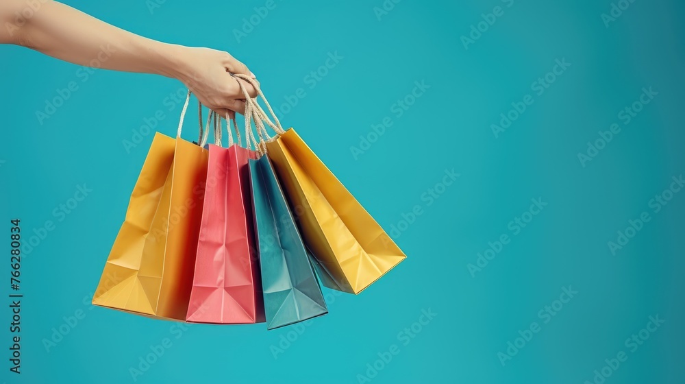 Colorful Shopping Spree, hand holding a vibrant array of shopping bags against a teal backdrop, symbolizing retail therapy and the joy of consumerism