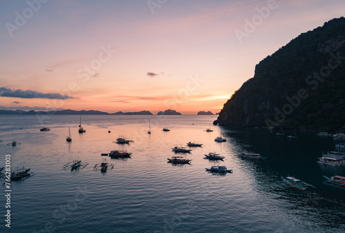 Aerial view of cliffs in the sea, yachts are sailing nearby, mountains covered with tropical forest. El Nido, Palawan, Philippines.