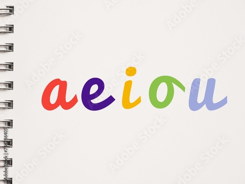 Colorful handwritten AEIOU lowercase vowels on a notebook photo