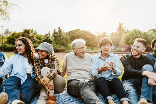 Happy multi generational people having fun sitting on grass in a public park - Diversity and friendship concept photo