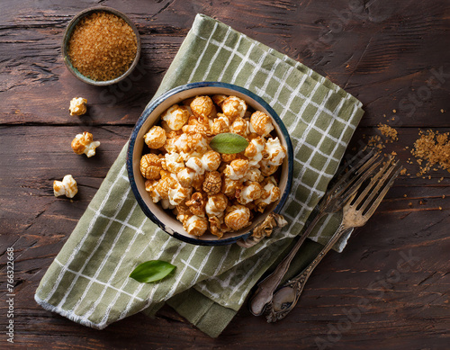 caramelized sweet popcorn served in vintage enameled bowl with brown sugar and textile napkin over dark wooden background