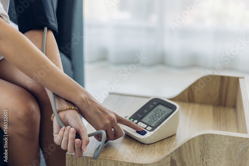 Woman measuring blood pressure by using digital sphygmomanometer at home. Woman using medical device to measure blood pressure. photo
