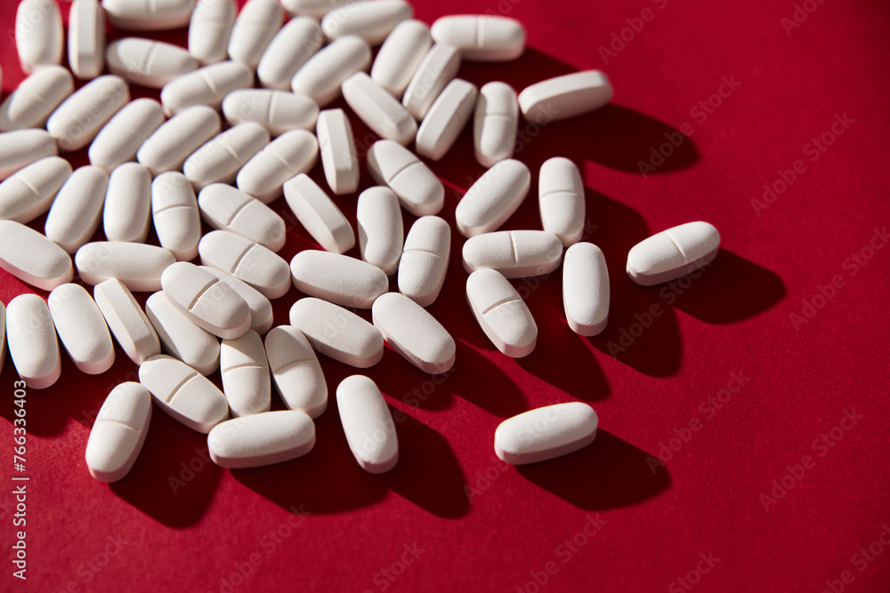 White Medical Pills on vibrant red background. 80s and 90s retro style, hard light and contrast shadows. Top view. White Medical Pills on vibrant red background. 80s and 90s retro style, hard light and contrast shadows. Top view.