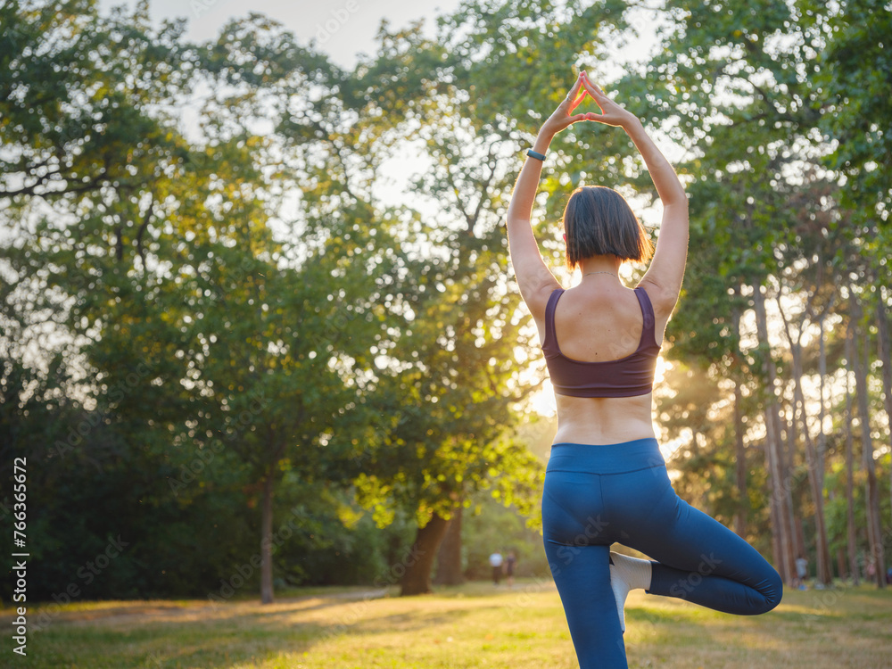 Young asian woman doing yoga in morning or evening at park, healthy woman relaxing and practicing tree pose at city park. Mindfulness, destress, Healthy habits and balance concept Young asian woman doing yoga in morning or evening at park, healthy woman relaxing and practicing tree pose at city park. Mindfulness, destress, Healthy habits and balance concept