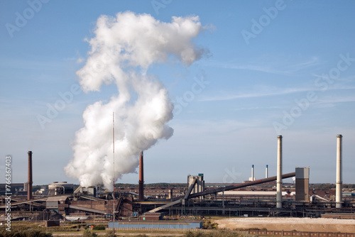 Rokende schoorstenen door staalproductie bij Tata Steel in Ijmuiden, tegen een blauwe lucht. photo