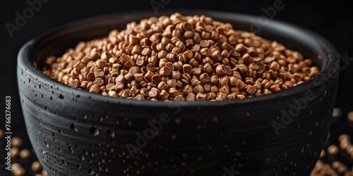 A bowl of brown grains is sitting on a black surface. The grains are scattered and appear to be of different sizes. The bowl is filled to the brim, and the grains are piled on top of each other