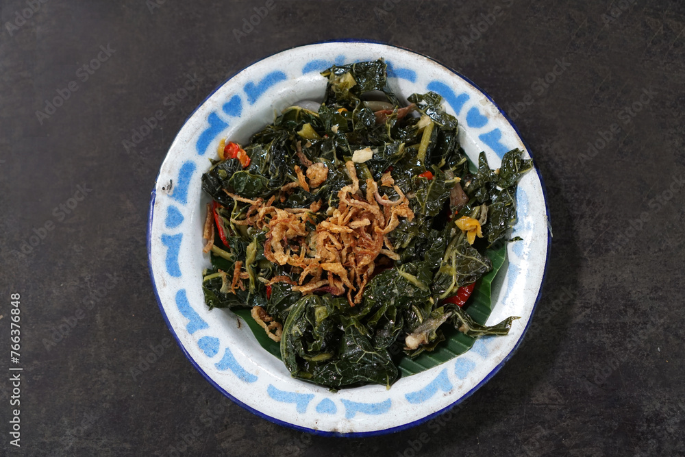 Stir-fried papaya leaves served on a classic plate on a wooden table Stir-fried papaya leaves served on a classic plate on a wooden table