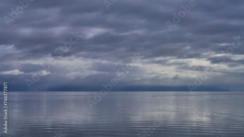 View over the calm ocean of an approaching rain storm with cloud reflections.