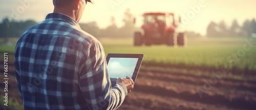 Modern farmer using tablet in field with blurred tractor and farm background