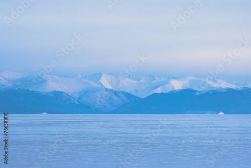 View of the mountains on the coast of ice-covered Lake Baikal. Beautiful winter landscape. Snow-capped mountain peaks in the distance. Barguzinsky ridge  Republic of Buryatia  Siberia  Russia.