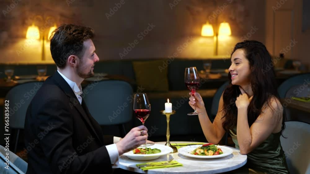 Happy romantic couple clinking with wine glasses while enjoying dinner in the restaurant. Lifestyle, love, relationships concept. Slow motion Happy romantic couple clinking with wine glasses while enjoying dinner in the restaurant. Lifestyle, love, relationships concept. Slow motion