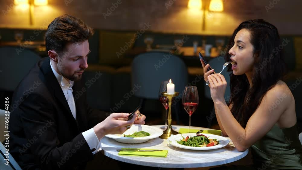 Smiling couple having date in the restaurant while eating salads and holding smartphones. Lifestyle, love, relationships concept. Slow motion Smiling couple having date in the restaurant while eating salads and holding smartphones. Lifestyle, love, relationships concept. Slow motion