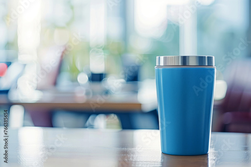 Blue insulated tumbler on wooden table in bright office with natural light