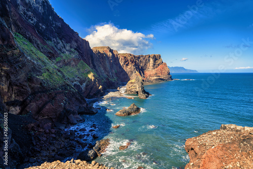 The picture showcases a picturesque rocky coastline with a dominant  tall rock rising from the azure waters of the ocean  under a clear sky. It s a scene full of tranquility and the majesty of nature.