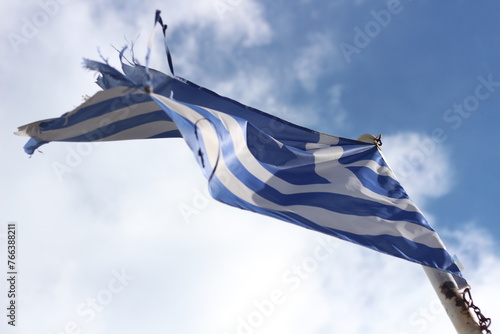 Resilience and Pride: Tattered Greek Flag Against Blue Sky