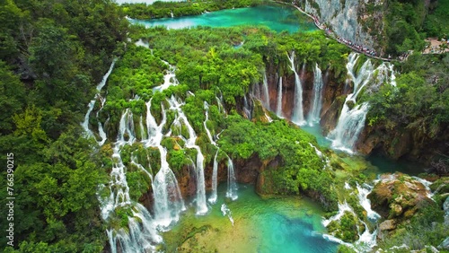 Crowd of tourists visit famous Plitvice waterfalls in Croatia. Summer landscape. Mountain streams flow into a lake with azure clear water.