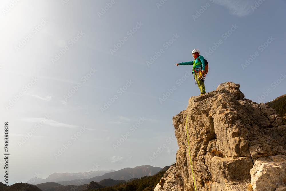 A person is standing on a rocky mountain top, pointing to the sky. Concept of adventure and exploration, as the person is likely a climber or mountaineer