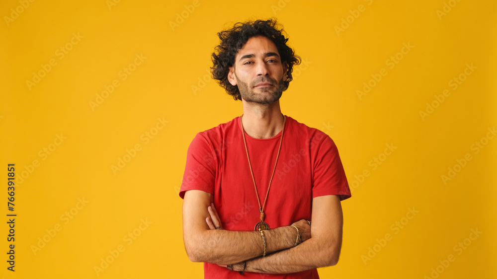 An attractive man with curly hair, dressed in red T-shirt, listens and agrees while looking at camera isolated on yellow background in studio An attractive man with curly hair, dressed in red T-shirt, listens and agrees while looking at camera isolated on yellow background in studio