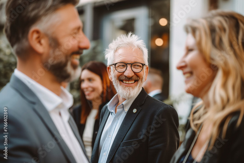 A business man with a beard and glasses is smiling at a group of people. The man is wearing a suit and tie