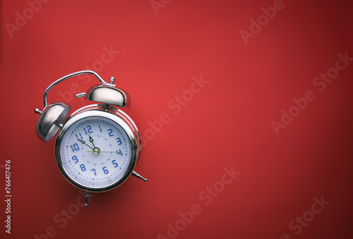 Wecker vor rotem Hintergrund mit Textfreiraum zeigt die Uhrzeit Fünf vor Zwölf photo