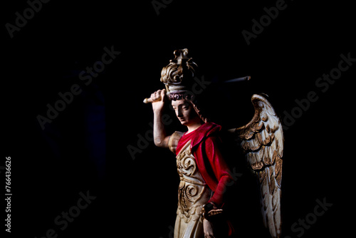  Saint Michael Archangel statue fighting the devil with sword in black background portrait 