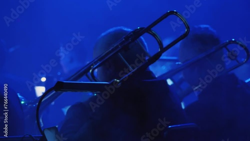 The musicians play trumpet and trombone in a brass band on a dimly lit stage. The blue tones and shadows create an intimate, moody atmosphere, emphasising the artistic character of the scene photo