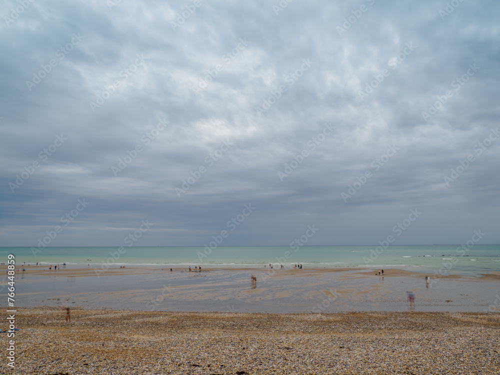 Landscape with dramatic sky. People walking on the shore and bathing in the sea. The sea coast between Audresselles and Ambleteuse. Waters of the English Channel - The La Manche Channel. France.
