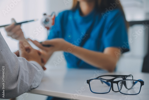 Close-up of Asian female doctor talking with elderly patient showing eyeball model and explaining eye disease in hospital