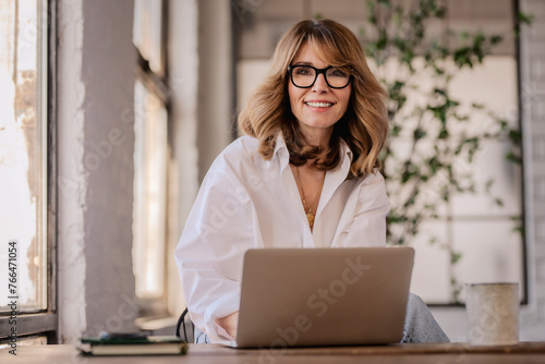 Attractive mid aged woman sitting at the table and using her laptop for work