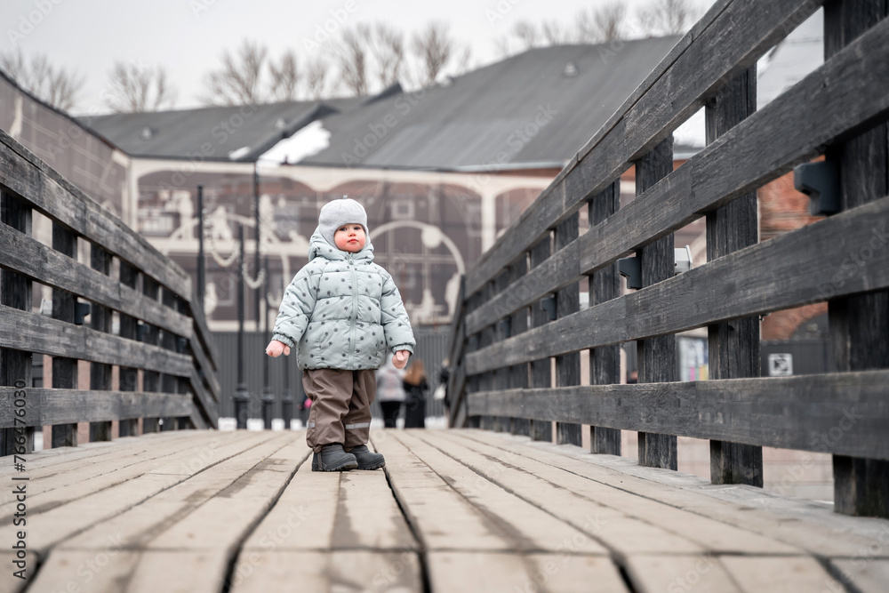 A little girl child toddler on a wooden bridge in the park in the cold season