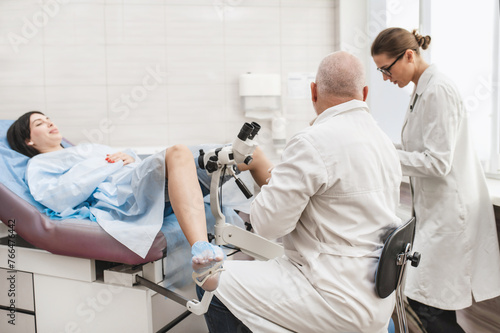 Man doctor look microscope at gynecologist's appointment, examining patient on chair with equipment. Colposcopy and Pap test. Doctor and nurse at medical appointment consultation Groop of three people