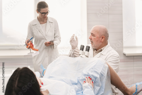 Man doctor look microscope at gynecologist's appointment, examining patient on chair with equipment. Colposcopy and Pap test. Doctor and nurse at medical appointment consultation Groop of three people