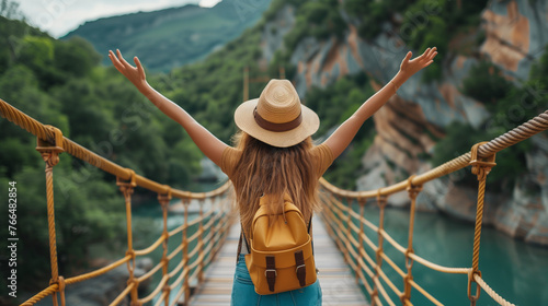 Happy travel woman with hat and backpack. Fun traveler who enjoys her trip and is ready for adventure. Nature landscape and a bridge, blurred background. © JMarques