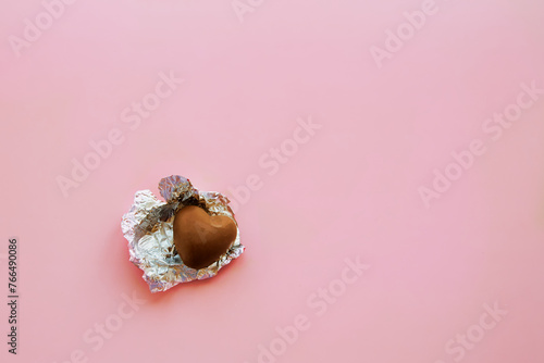 A single milk chocolate candy in an unwrapped wrapper lies on a pink background, the last candy, an open heart, a lonely heart, the last chance