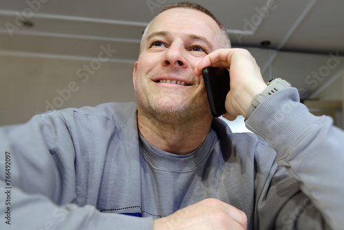 A cheerful man is captured enjoying a conversation on a mobile phone. The sincere smile on his face reflects the positive nature of the conversation