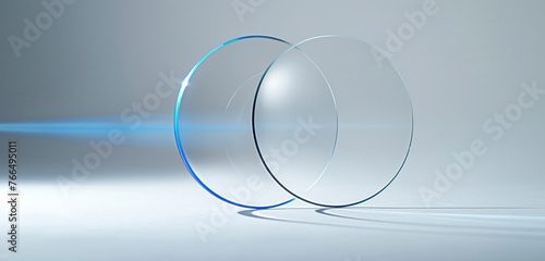 An optically clear, thin fu ll glass circle, seen from a side angle with a rotated perspective. a blue line of light shines through the circle and stands against a pristine white background photo