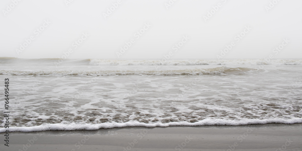Waves of ocean on a Misty morning creating foam on sandy sea beach of grey color. Waves of ocean on a Misty morning creating foam on sandy sea beach of grey color.