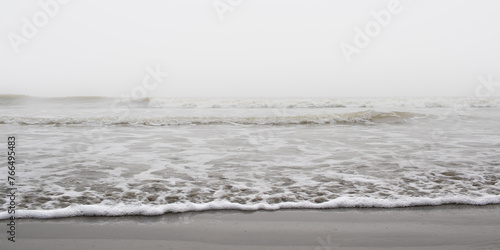 Fototapeta Naklejka Na Ścianę i Meble -  Waves of ocean on a Misty morning creating foam on sandy sea beach of grey color. 