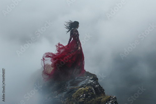 Woman wearing luxurious dress standing on rock in fog 