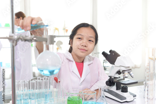 Cute young scientist schoolgirl in lab coat do science experiments. Student girl use equipment to study chemistry in school laboratory. Happy child has fun experiment. Kid learning science education.
