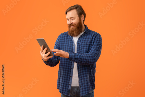 Redhaired bearded man websurfing on digital tablet on orange background