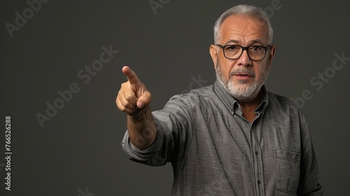 Senior man in gray shirt pointing with index finger to important information on copy space. Man pointing at something on gray background, closeup of hand