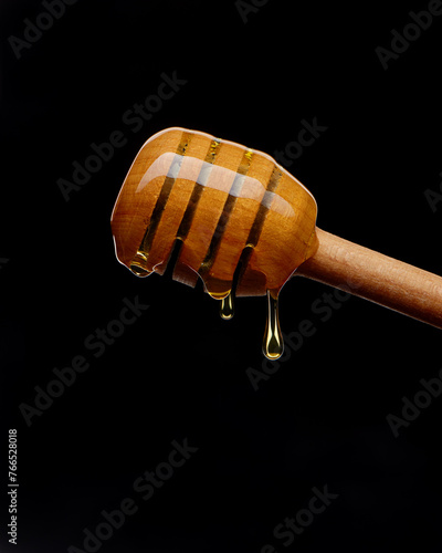 Liquid honey dripping from wooden spoon on black background