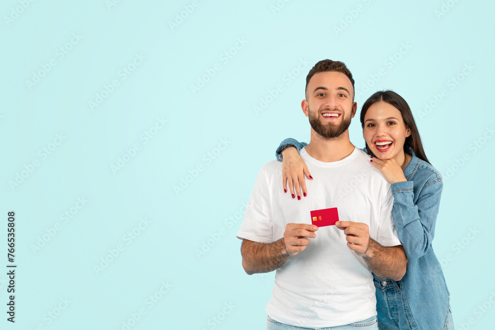 Happy European couple holds credit card against blue backdrop Happy European couple holds credit card against blue backdrop