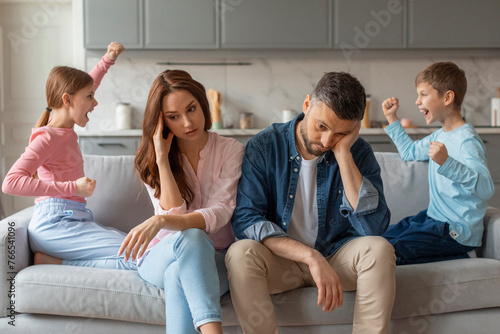 Fotografia Two preteen children screaming at each other, stressed parents sitting beside th