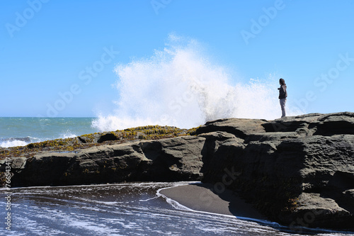 Young man on a rock watching splashing wave on the Beach of Pelline during summer (Maule region, Chile)