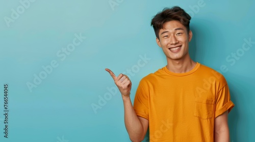 Happy young man in yellow t-shirt pointing to copy space on a blue background. Advertisement concept photo