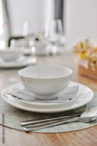 Close up white porcelain tableware plates on place mats and empty wine glasses ready for dinner. Table settings wait for guests at home or restaurant. No people
